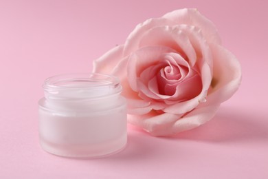 Moisturizing cream in open jar and rose flower on pink background. Body care product