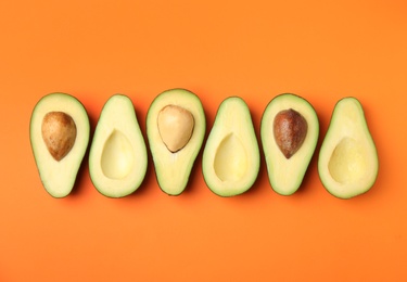 Cut fresh ripe avocados on orange background, flat lay