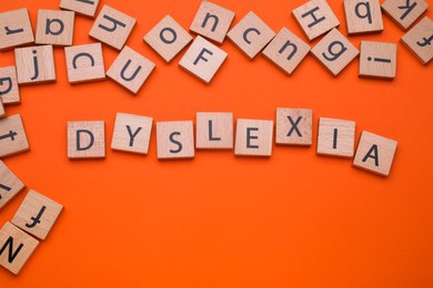 Photo of Wooden cubes with word Dyslexia on orange background, flat lay