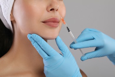 Photo of Doctor giving facial injection to young woman on light grey background, closeup. Cosmetic surgery