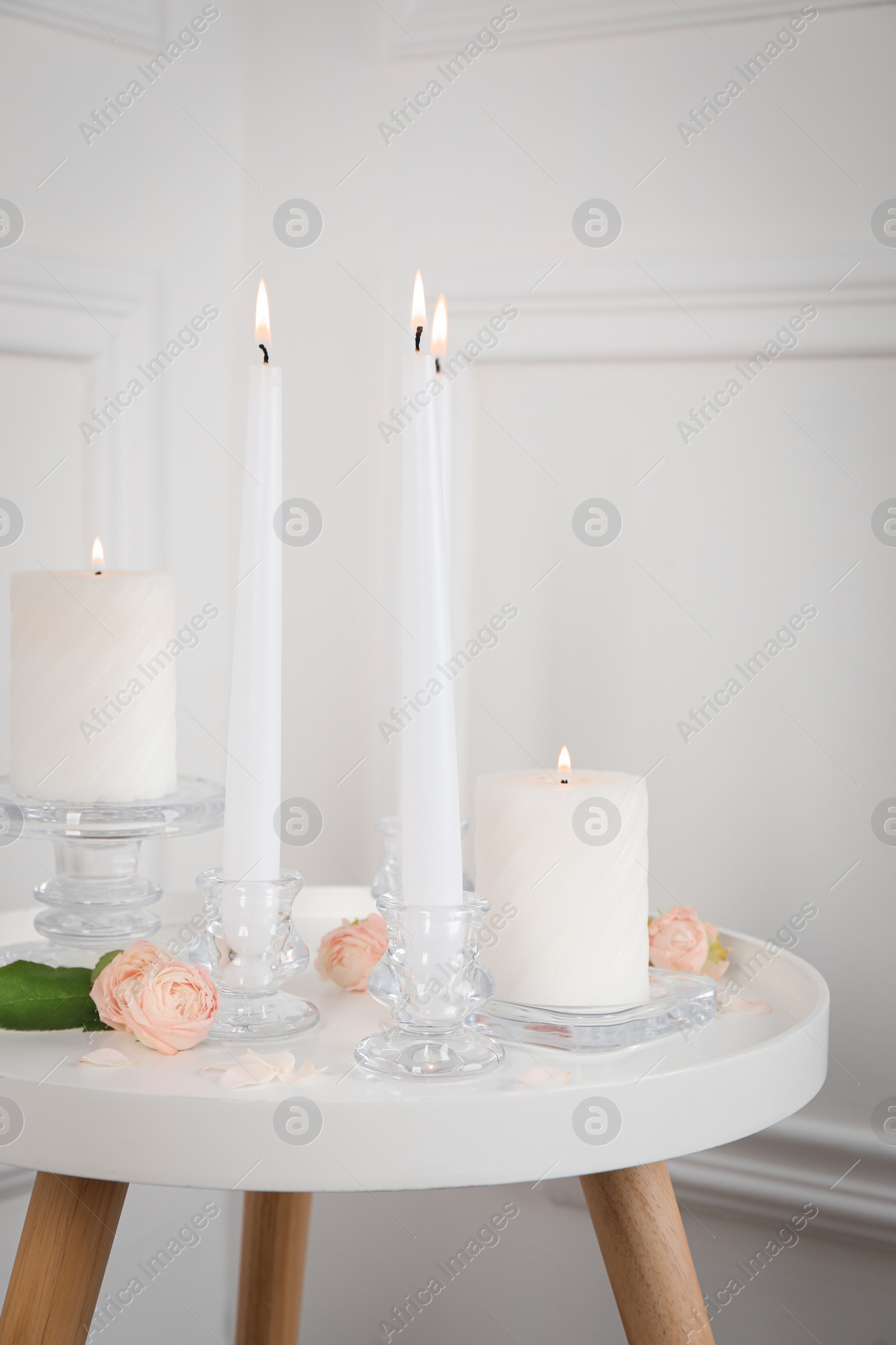 Photo of Elegant candlesticks with burning candles and flowers on white table