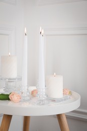 Elegant candlesticks with burning candles and flowers on white table