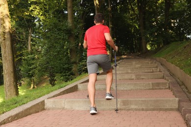 Photo of Man practicing Nordic walking with poles on steps outdoors, back view
