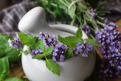 Photo of Mortar with fresh lavender flowers, mint and pestle on table, closeup