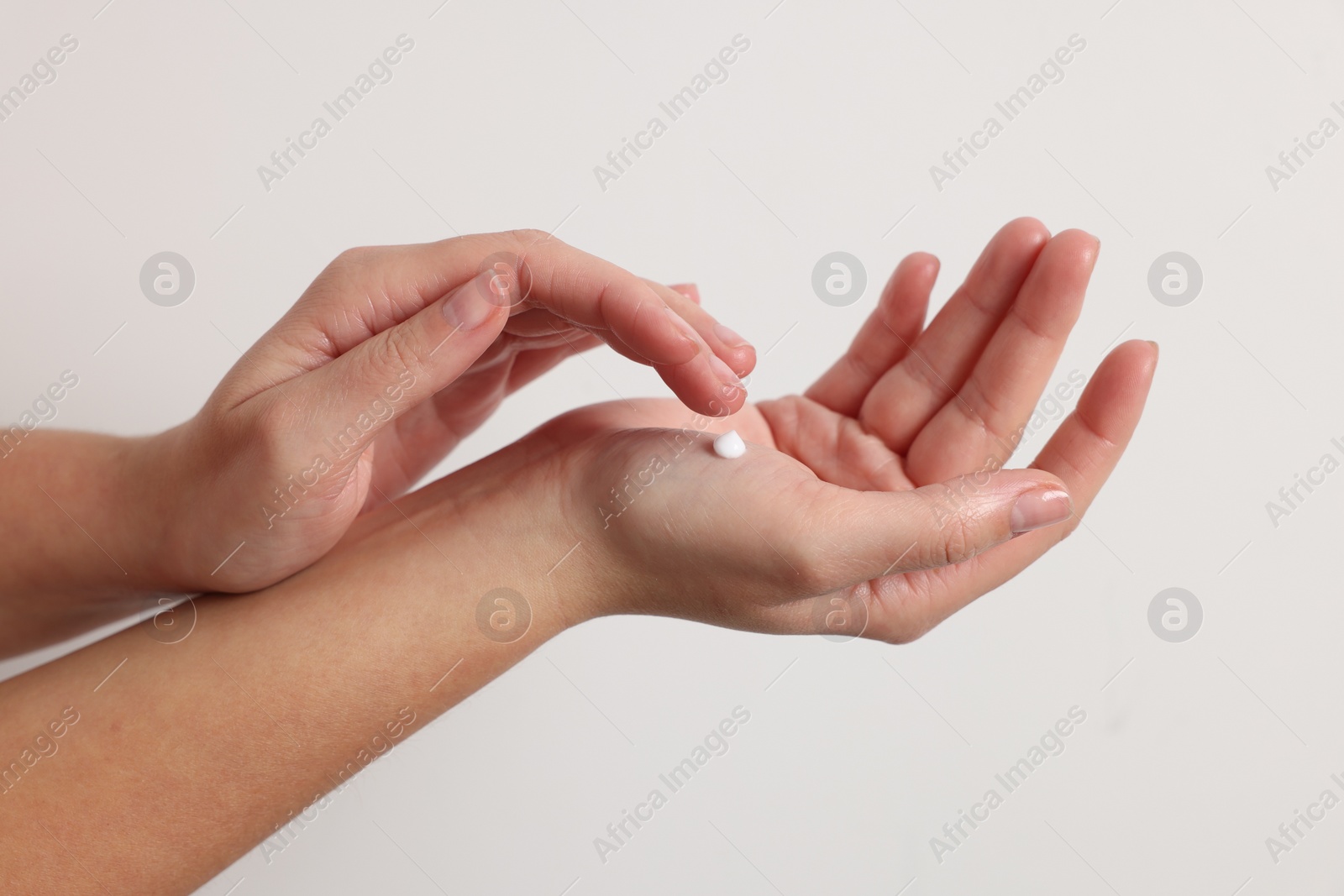 Photo of Woman applying cosmetic cream onto hand on white background, closeup