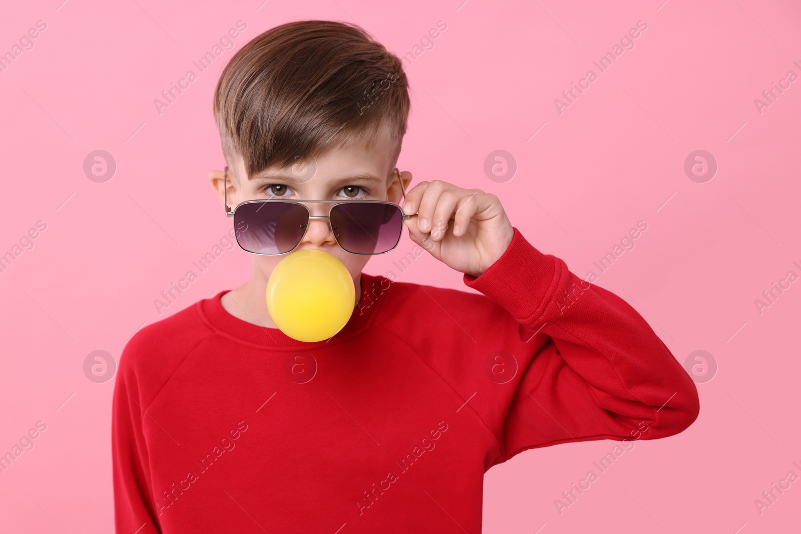 Photo of Boy in sunglasses blowing bubble gum on pink background