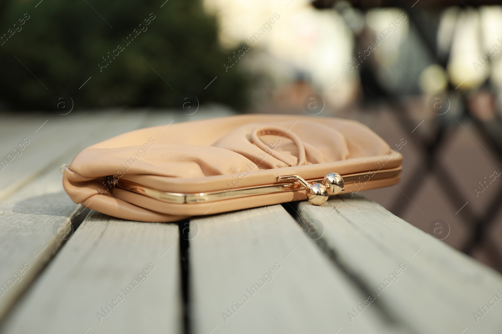 Photo of Beige leather purse on wooden bench outdoors, closeup. Lost and found