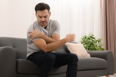 Photo of Man suffering from pain in his shoulder on sofa indoors