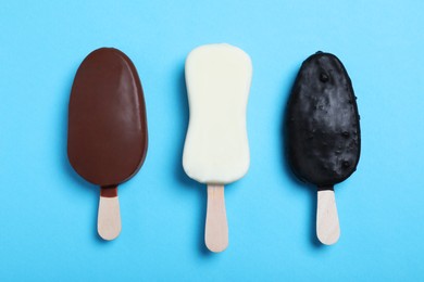 Different glazed ice cream bars in light blue background, flat lay