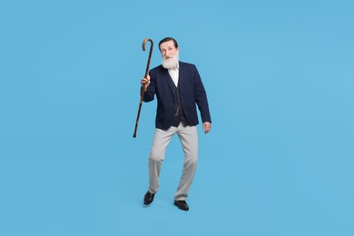 Cheerful senior man with walking cane on light blue background