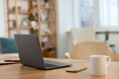 Photo of Cozy workspace with laptop, cup of coffee and smartphone on wooden desk at home