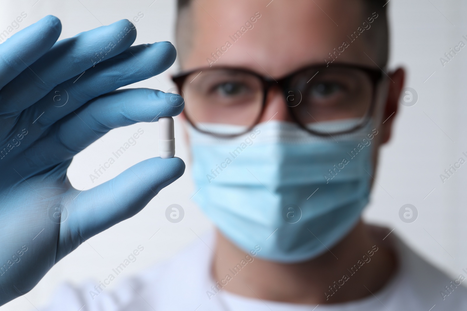 Photo of Doctor holding pill on light background, selective focus. Space for text