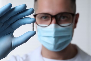 Doctor holding pill on light background, selective focus. Space for text