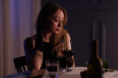 Photo of Elegant young woman with glass of wine at table indoors in evening