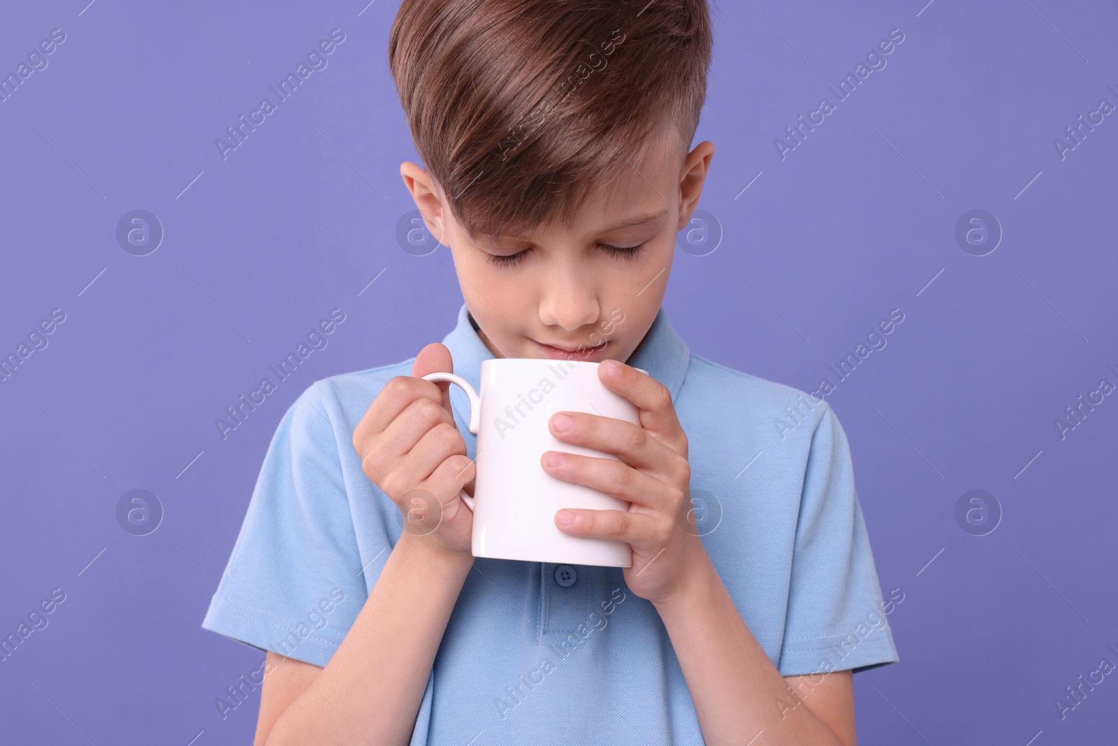 Photo of Cute boy drinking from white ceramic mug on violet background