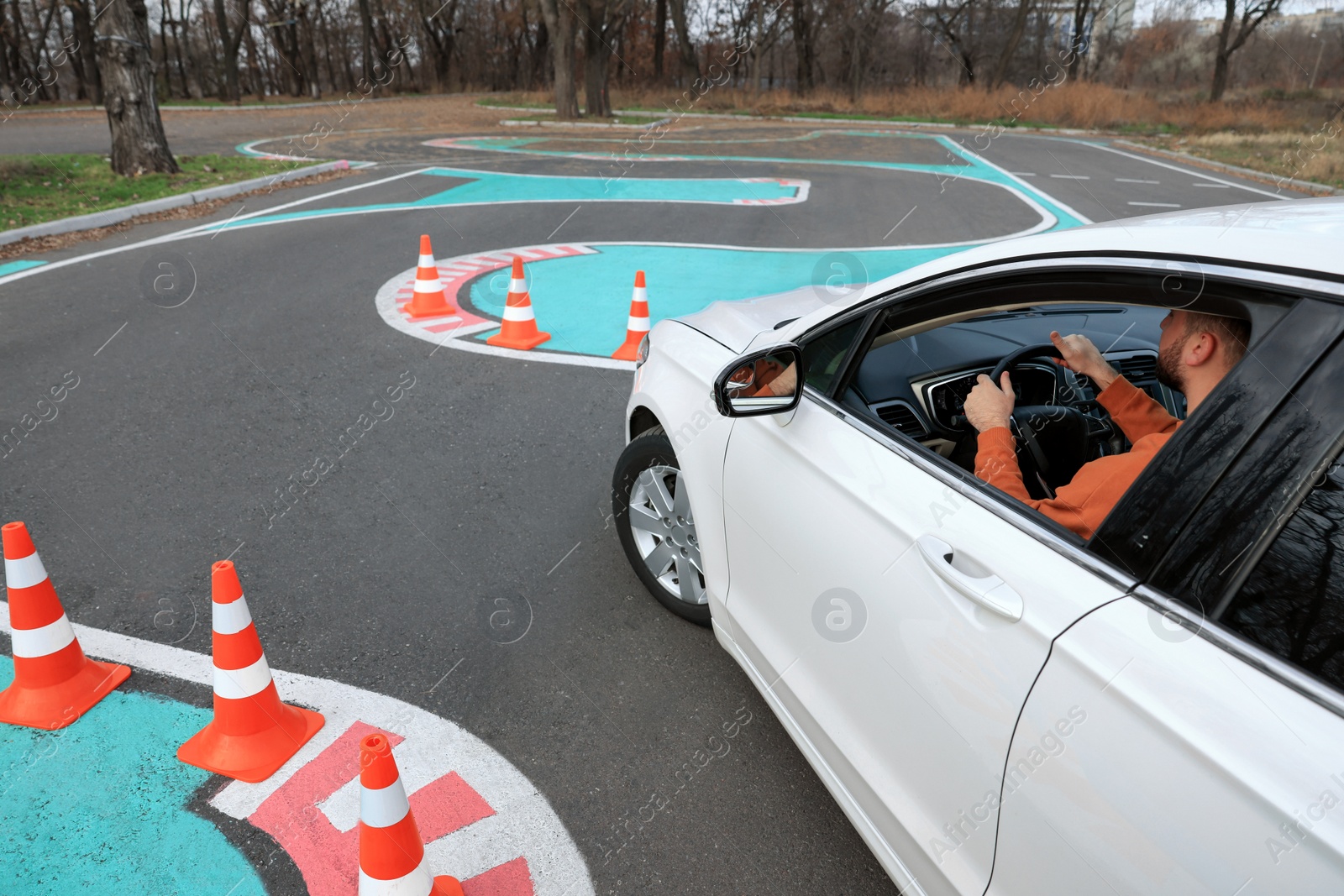 Photo of Young man in car on test track with traffic cones, above view. Driving school