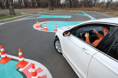 Young man in car on test track with traffic cones, above view. Driving school