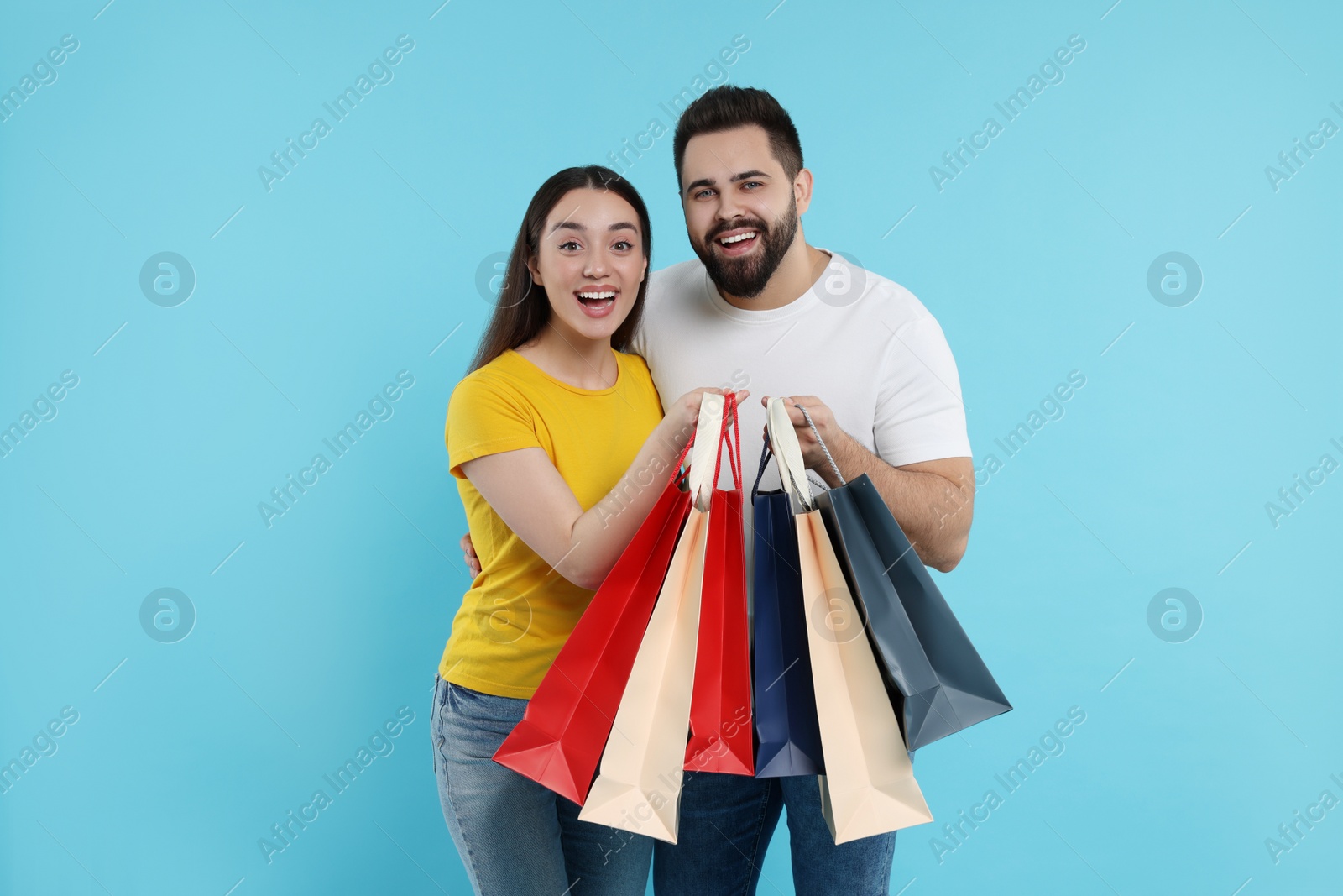 Photo of Excited couple with shopping bags on light blue background