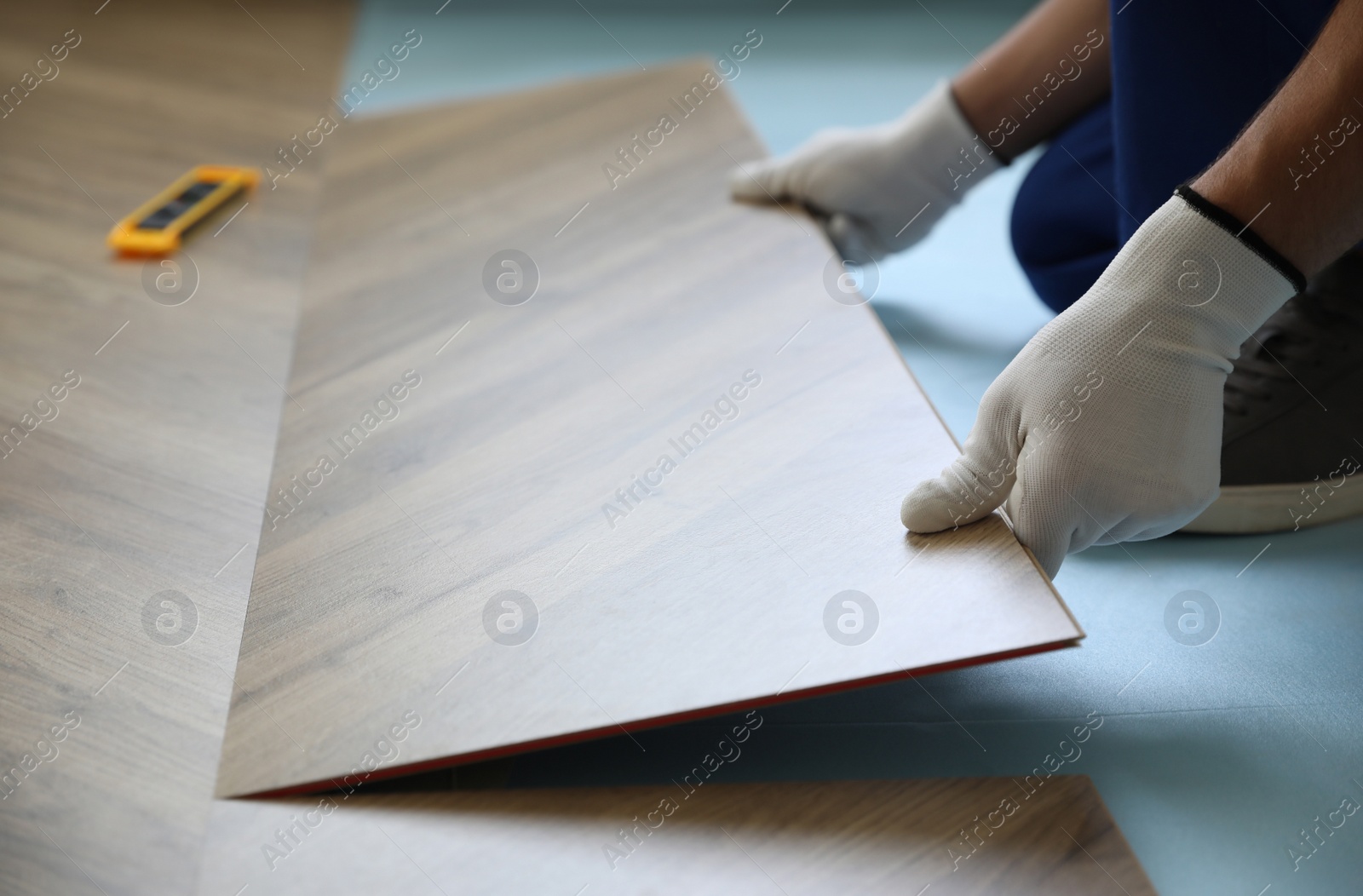 Photo of Worker installing laminated wooden floor indoors, closeup