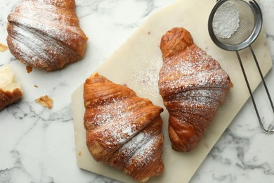 Photo of Tasty croissants with powdered sugar on white marble table, flat lay