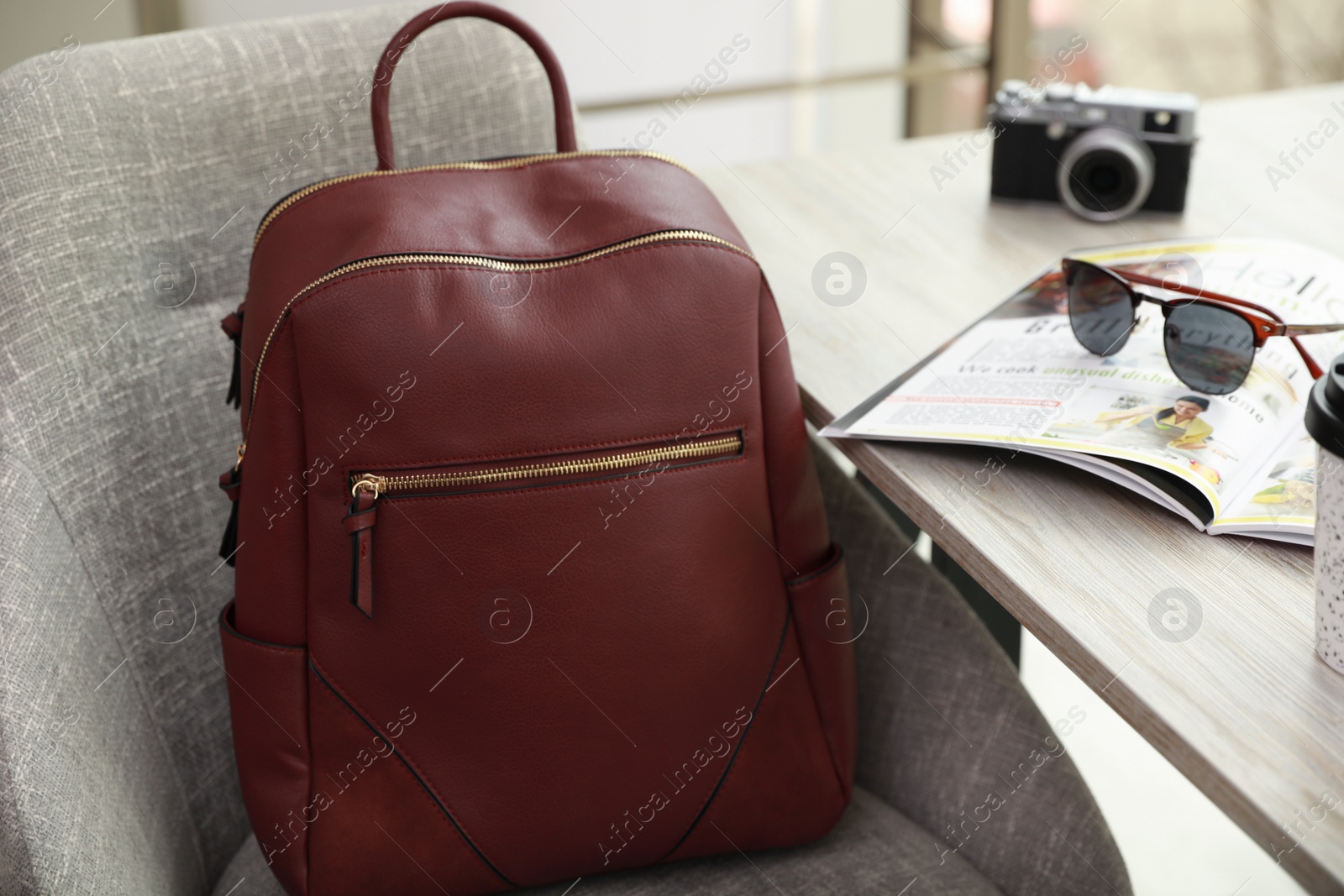 Photo of Stylish backpack on grey chair near table indoors