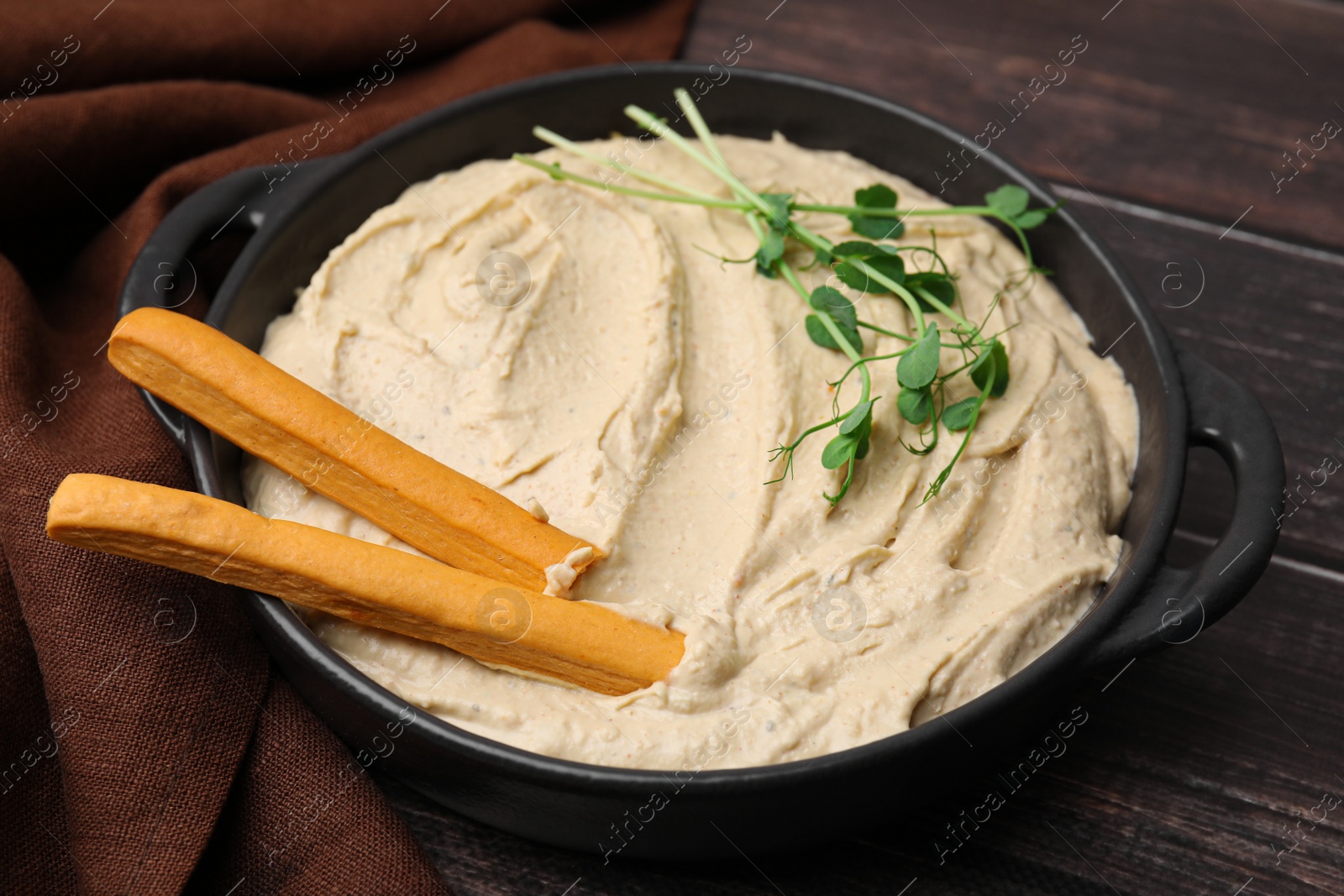Photo of Delicious hummus with grissini sticks on wooden table, closeup