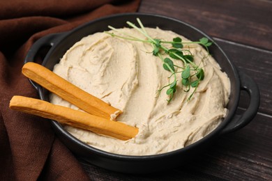 Photo of Delicious hummus with grissini sticks on wooden table, closeup