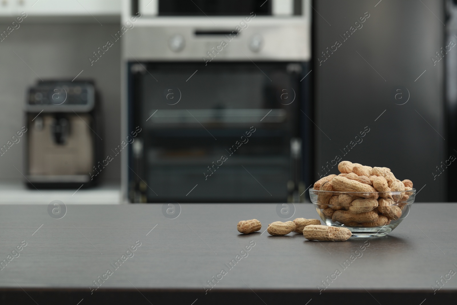 Photo of Glass bowl of peanuts on grey table in kitchen. Space for text