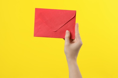 Woman holding red paper envelope on yellow background, closeup