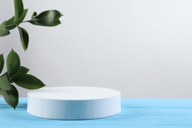 Photo of Green leaves and round shaped podium on light blue wooden table against white background. Space for text