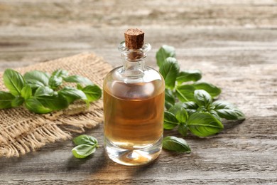 Glass bottle of basil essential oil and leaves on wooden table