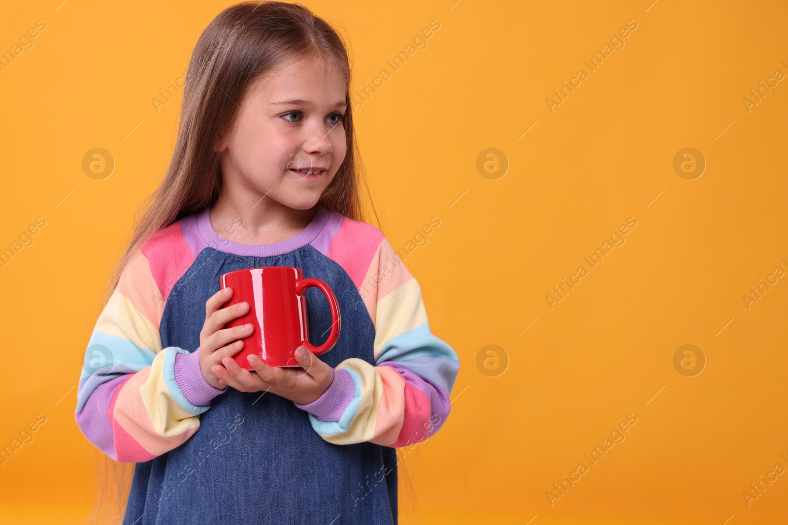 Photo of Cute girl with red ceramic mug on orange background, space for text