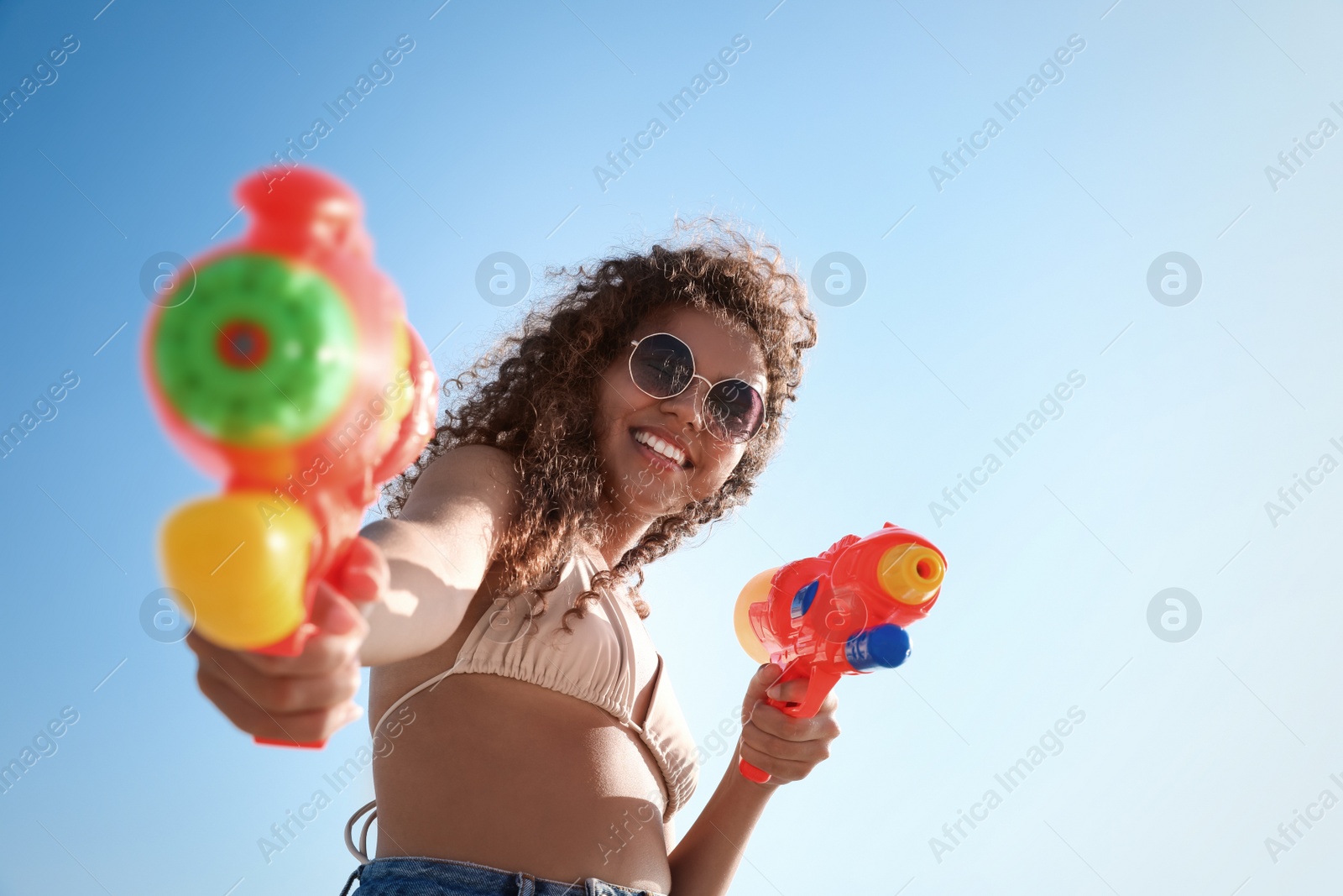 Photo of African American woman with water guns against blue sky, low angle view