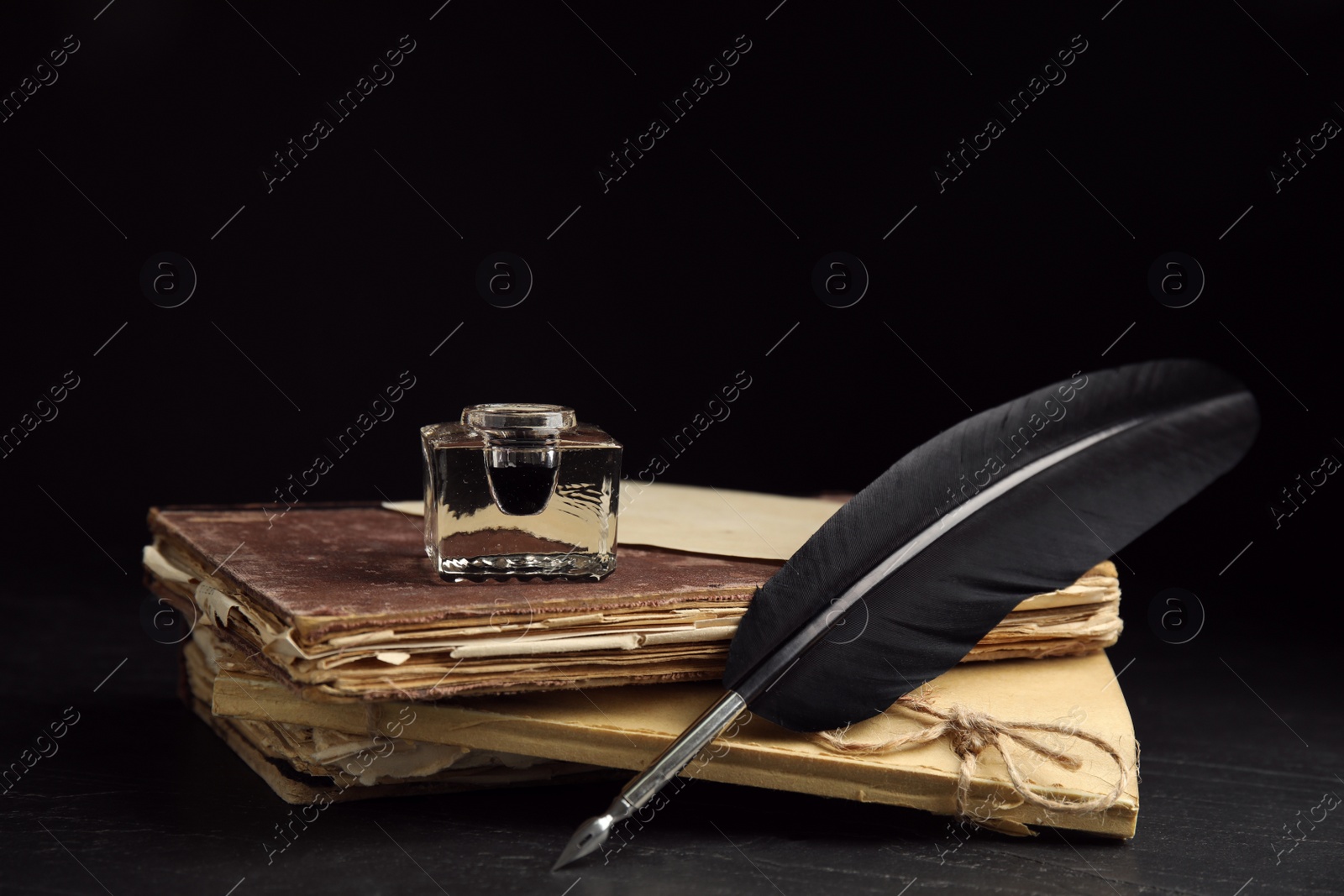 Photo of Feather pen, inkwell and old books on black table