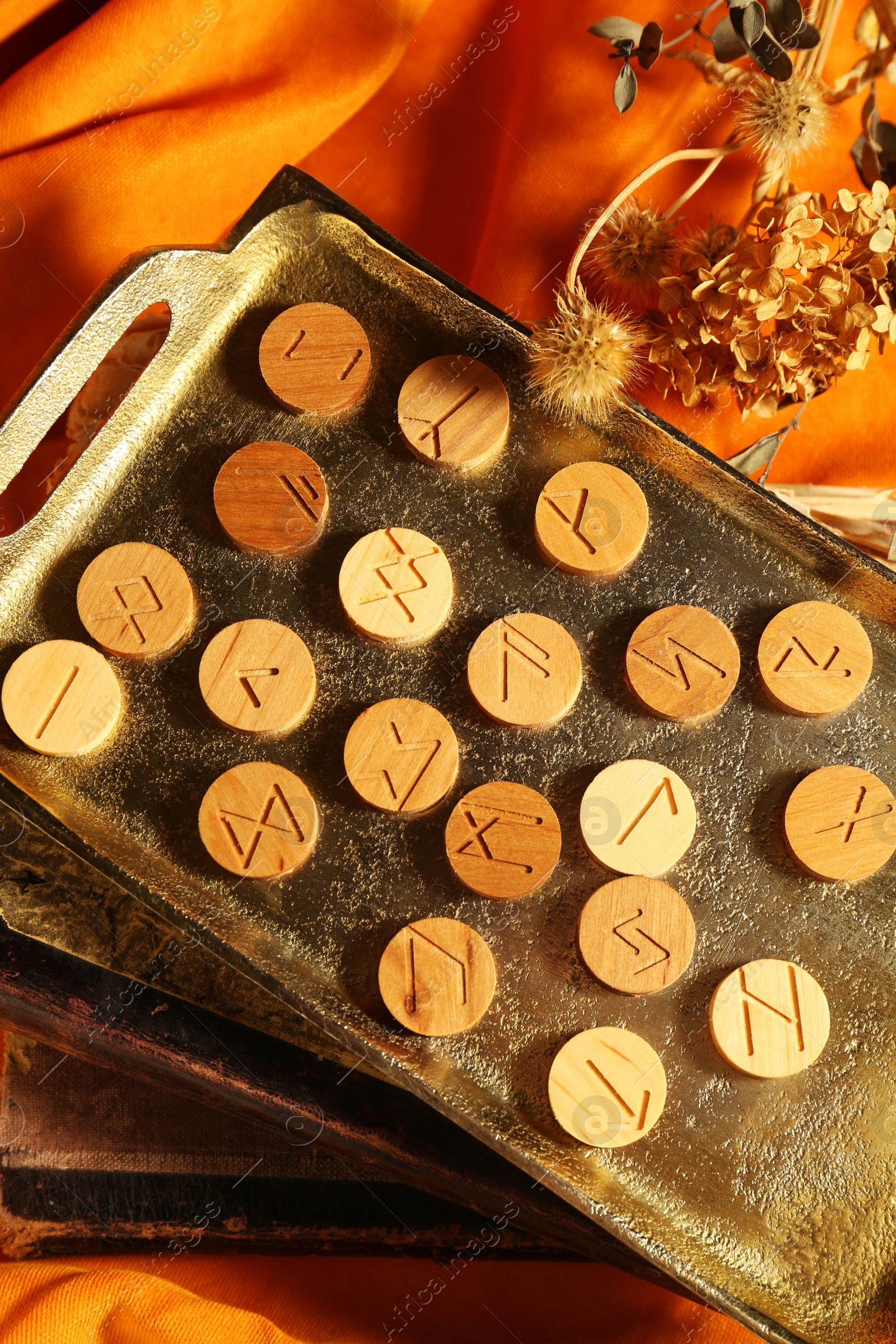 Photo of Tray with wooden runes, dried flowers and old books on orange fabric, top view