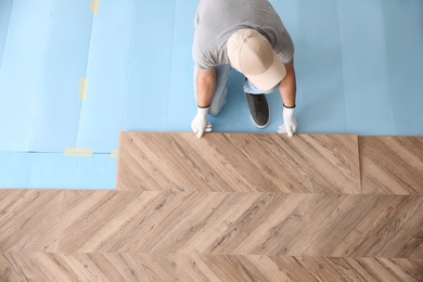 Photo of Worker installing laminated wooden floor indoors, above view