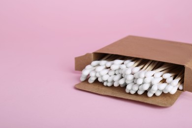 Photo of Box with wooden cotton buds on pink background. Space for text