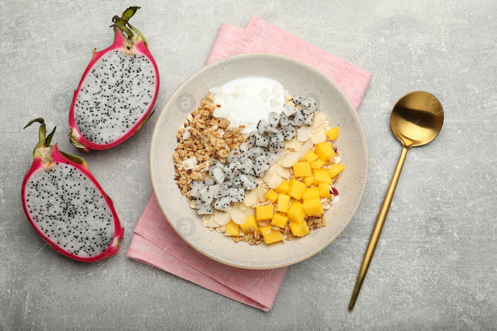 Photo of Bowl of granola with pitahaya, mango and yogurt served on light grey table, flat lay