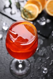 Photo of Glass of tasty Aperol spritz cocktail with orange slices and ice cubes on dark gray table, above view