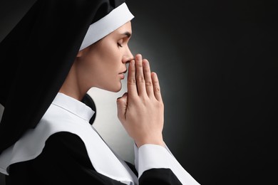 Photo of Nun with clasped hands praying to God on black background. Space for text