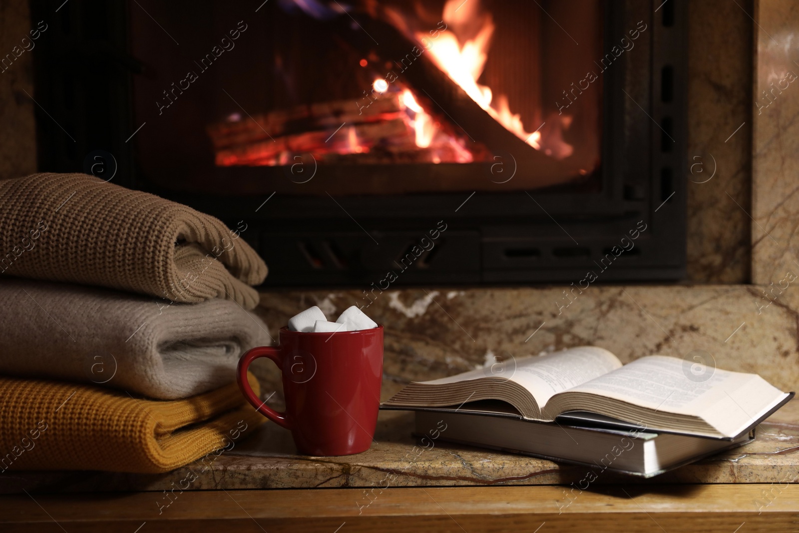 Photo of Stack of warm sweaters, cup, books and fireplace indoors