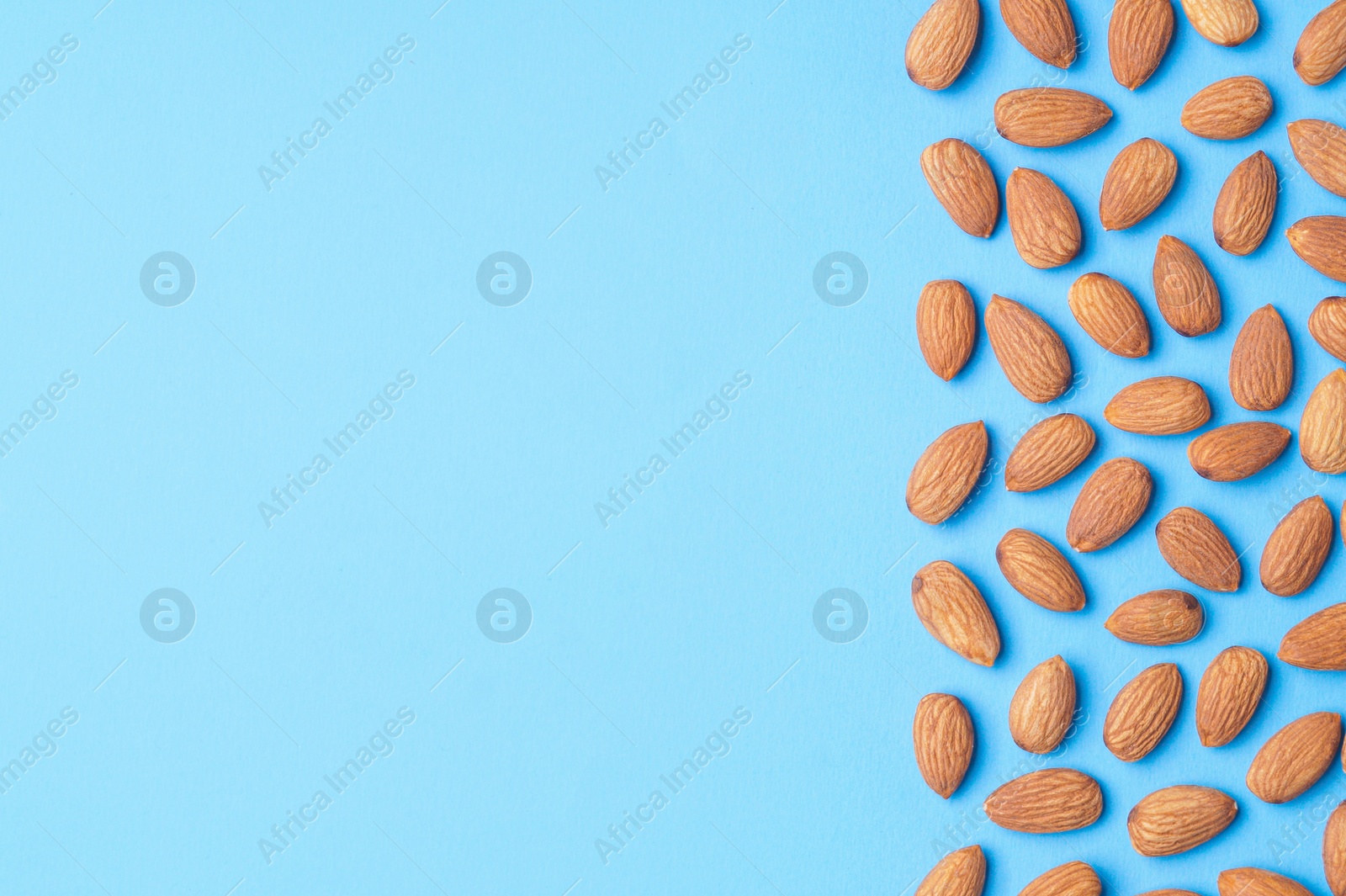 Photo of Delicious raw almonds on light blue background, flat lay. Space for text