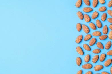 Photo of Delicious raw almonds on light blue background, flat lay. Space for text