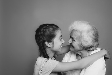 Cute girl hugging her grandmother on grey background. Black and white photography