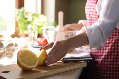 Woman with fresh cut lemon at countertop in kitchen, closeup