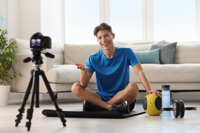 Photo of Smiling sports blogger recording fitness lesson with camera at home