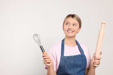 Photo of Beautiful young woman in clean apron with kitchen tools on light grey background. Space for text