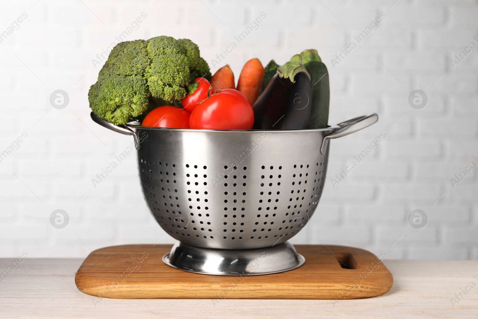 Photo of Fresh vegetables in colander on white wooden table