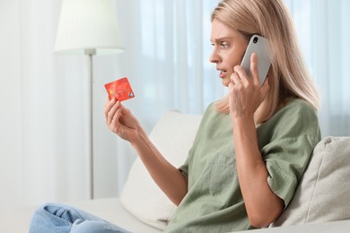 Photo of Stressed woman with credit card talking on smartphone at home. Be careful - fraud