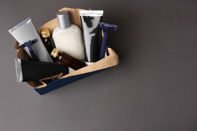 Box with different men's shaving accessories and cosmetics on dark grey background, top view. Space for text